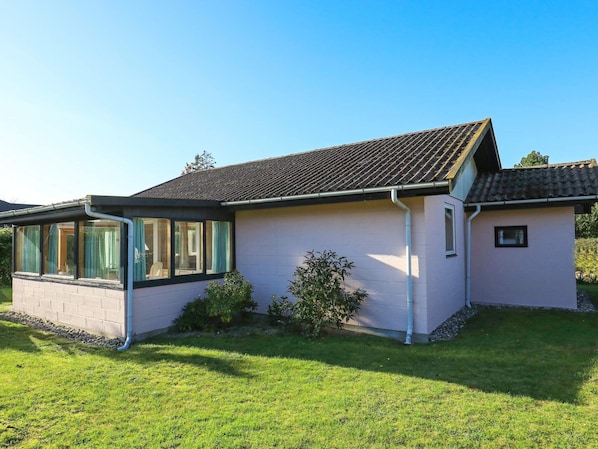 A single-story house with a sloped roof, a covered porch with glass doors, and a small garden area.