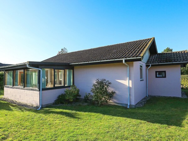 A single-story house with a tiled roof, a covered porch with glass doors, and a small garden area. - 5 Person Holiday Home in Vaeggerlose (Vaeggerlose)