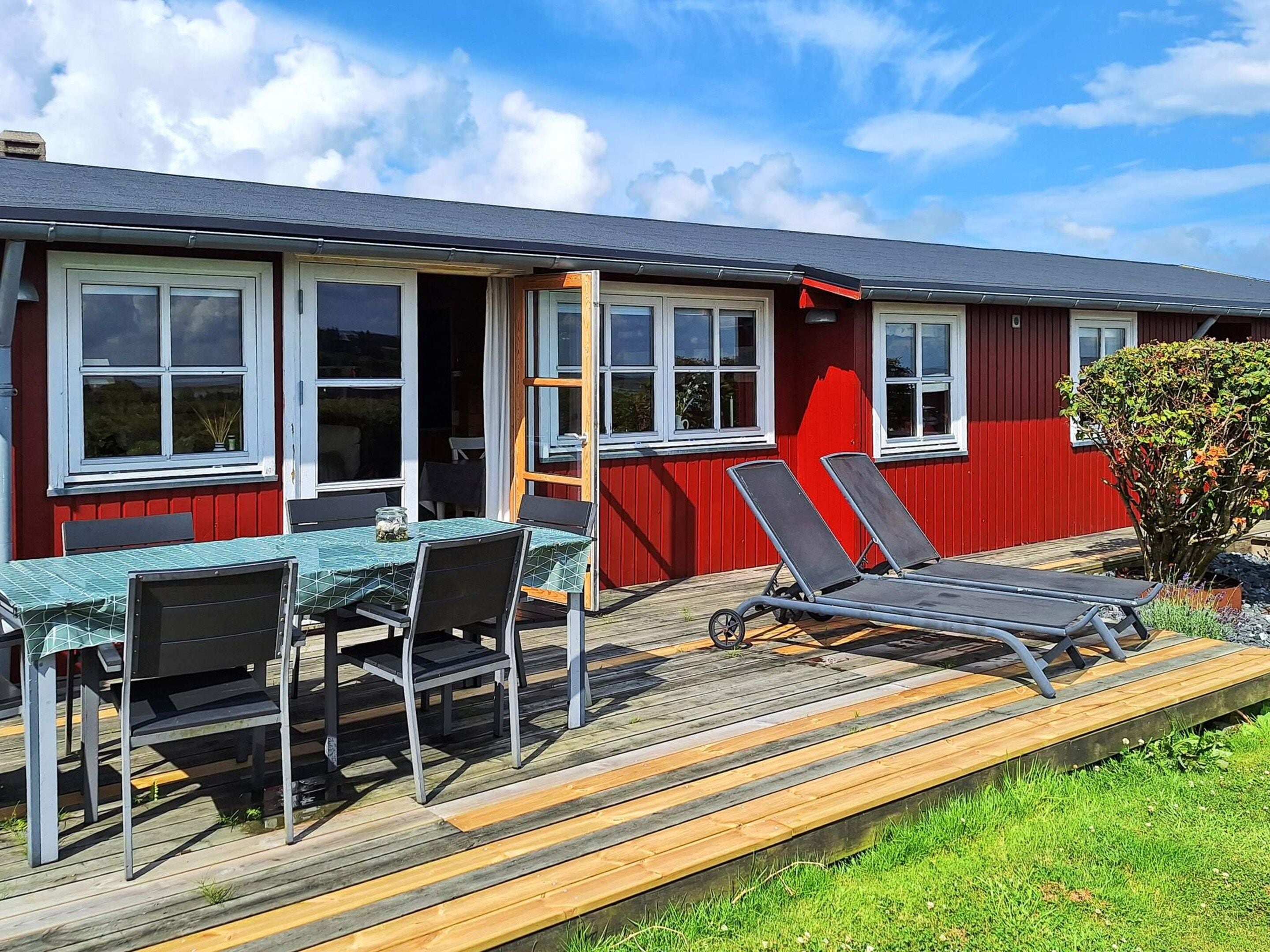 Een rood gebouw met een terras, een tafel met stoelen en twee ligbedden.