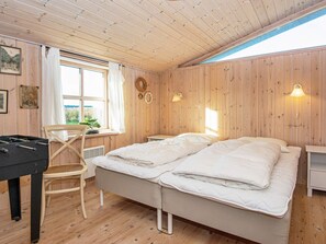 A room with wooden walls, a bed with white bedding, a desk with a computer, a chair, and a window with curtains.