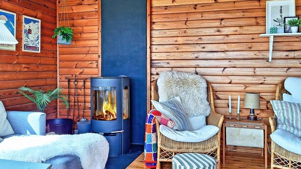 A cozy cabin interior with a wood-burning stove, wicker furniture, and a blue accent wall. - 6 Person Holiday Home in Lemvig (Lemvig)