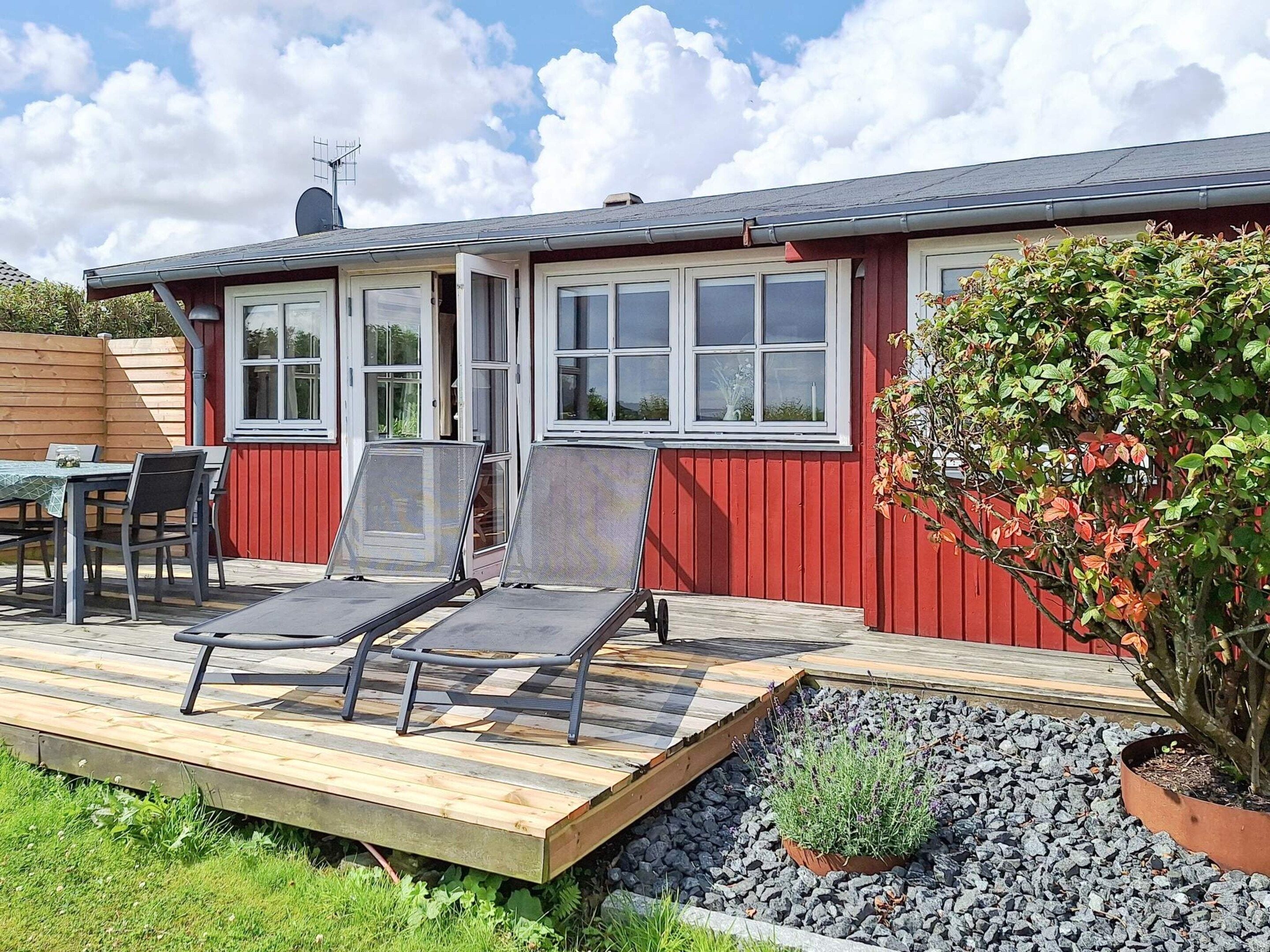 A red building with a deck, outdoor seating, and a potted plant.