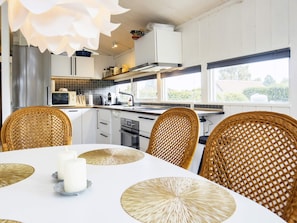 A modern kitchen with white cabinets, a stainless steel refrigerator, a microwave, and a stove. There are wicker chairs around a table with a white tablecloth and candles. - Tasteful Holiday Home in KarrebÃ¦ksminde near Sea (Karrebæksminde)