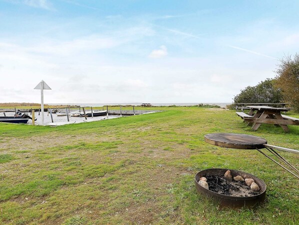 A grassy area with a barbecue grill, picnic tables, and a view of the water with boats. - Scenic Fjord Retreat-by Traum (Vemb)