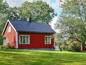 A red wooden house with a dark tiled roof, white windows, and a chimney.