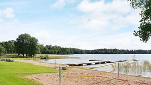 A beach volleyball court with a net, a picnic table, and a dock by the lake.