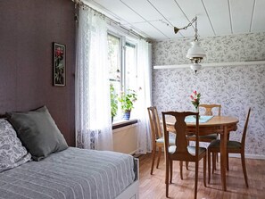 A bedroom with a bed, a window with curtains, a radiator, a dining table with chairs, and a wall with floral wallpaper. - 6 Person Holiday Home in Ed (Ed)