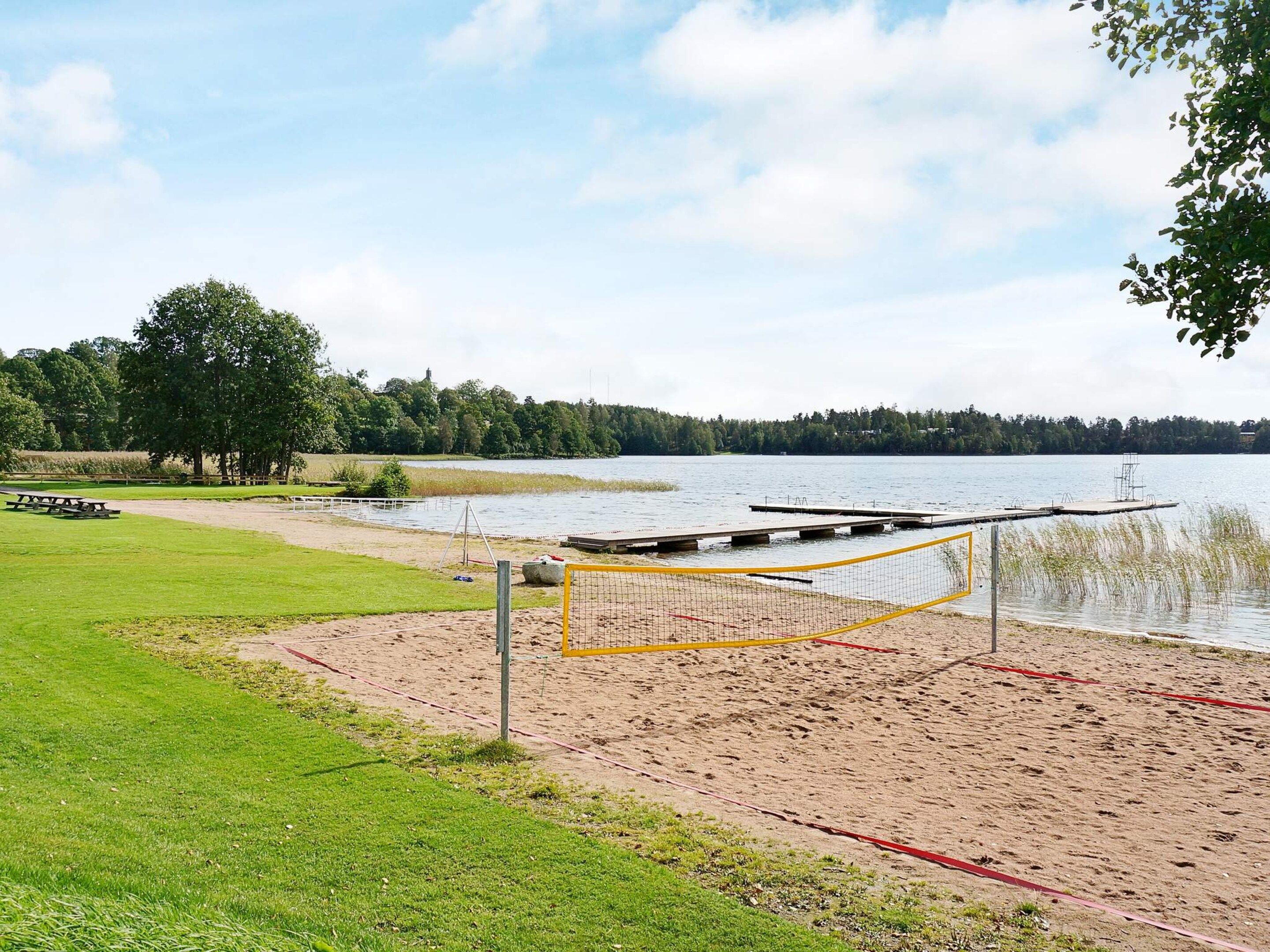 A beach volleyball court with a net, a picnic table, and a dock extending into a lake.