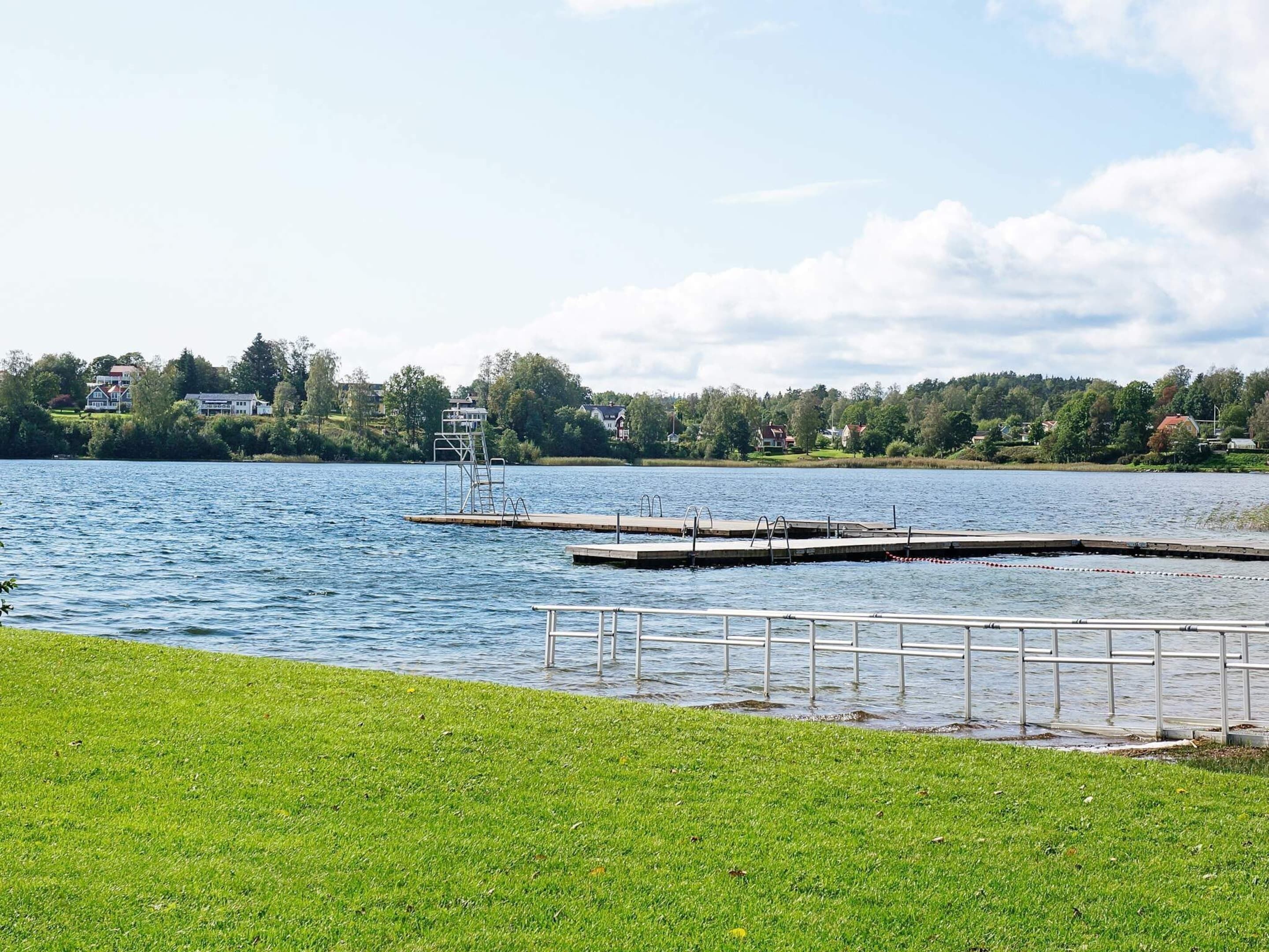 Une vue sur le lac, avec une zone herbeuse, un quai et des maisons en arrière-plan.