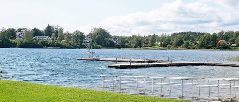 Une vue sur le lac, avec une zone herbeuse, un quai et des maisons en arrière-plan.