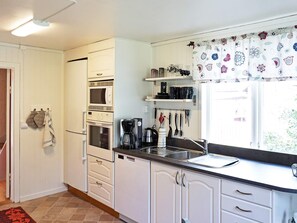 A compact kitchen with white cabinetry, a built-in oven, a coffee maker, and a window with patterned curtains.
