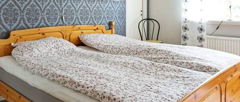 A double bed with a floral bedspread, a wooden headboard, and a patterned wall.