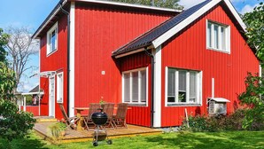 A red house with a wooden deck, a barbecue grill, and a large window.