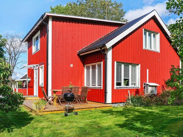 A red house with a wooden deck, a barbecue grill, and a large window.