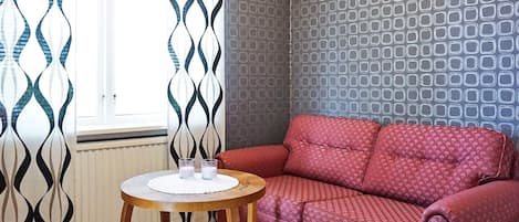 A cozy living room with a red patterned sofa, a small wooden table with glasses, and patterned curtains.