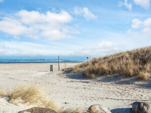 Una playa con arena, césped y un poste de madera.