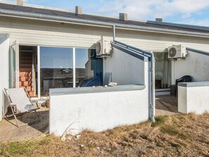Un edificio residencial con un patio cubierto, un cerramiento de vidrio corredero que da a un patio de ladrillo, y un equipo de aire acondicionado instalado en la pared exterior.