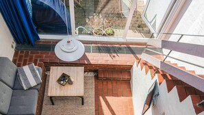 Un patio iluminado por el sol con un sofá gris, un tapete tejido y una pequeña mesa con una cesta y piedras.