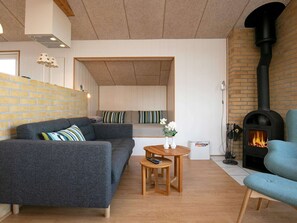 A cozy living room with a sofa, a small wooden table, a blue armchair, a fireplace, and a brick wall. - Cozy Holiday Home in Funen near Sea (Frørup)