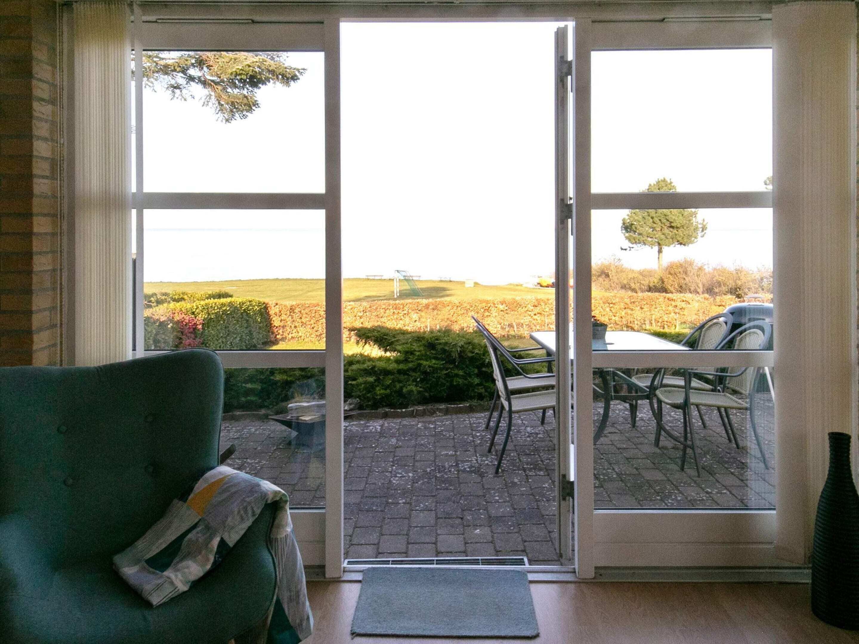 A room with a green armchair, a table, and chairs outside a sliding glass door.