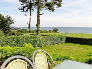 A patio with wicker chairs, a table, and a view of the sea. - Cozy Holiday Home in Funen near Sea (Frørup)