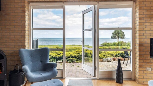 A modern living room with a large sliding glass door leading to a balcony with a view of the sea. - Cozy Holiday Home in Funen near Sea (Frørup)