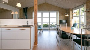 A modern kitchen with a central island, a dining area with a round table and chairs, and large windows allowing natural light. - Cozy Holiday Home in Funen near Sea (Frørup)