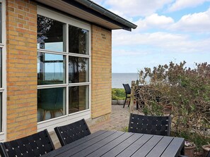 A brick building with large windows, a patio with a table and chairs, and a view of the sea. - Cozy Holiday Home in Funen near Sea (Frørup)