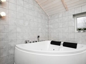A modern bathroom with a freestanding bathtub, tiled walls, and a window with plants.