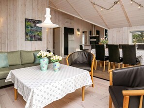 Una habitación acogedora con techo de madera, una mesa de comedor con sillas, un sofá y un jarrón con flores.