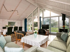 A spacious room with a high ceiling, a dining area with a table and chairs, a sofa, and a television.