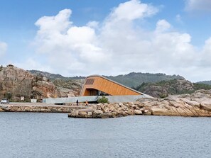 A modern building with a curved roof, situated by a rocky shoreline. - Holiday Home in Lindesnesnes (Lindesnes)