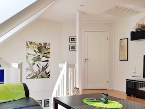 A living room with a high ceiling, a staircase, a dining table with a green placemat, and a television on a black stand. - Holiday Home in Lindesnesnes (Lindesnes)