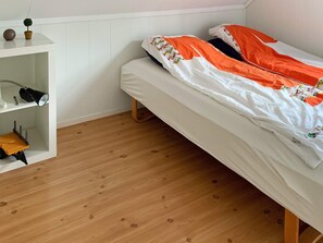 A small, neatly arranged bedroom with a single bed, a shelf unit with a lamp, and a small table with a plant. - Holiday Home in Lindesnesnes (Lindesnes)