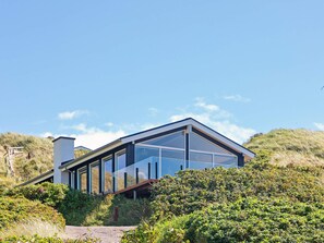A modern house with large glass windows, a sloped roof, and surrounded by lush greenery. - 6 Person Holiday Home in Lokken (Lokken)
