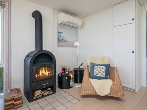 A cozy room with a wood-burning stove, a wicker chair with a fluffy pillow, and a lamp. - 6 Person Holiday Home in Lokken (Lokken)