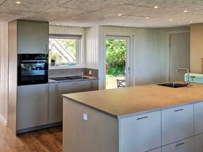 Une cuisine moderne dotée d’un îlot central, d’appareils électroménagers intégrés et donnant sur un espace extérieur.