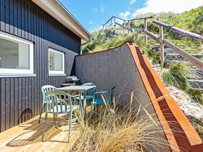 A modern outdoor seating area with a table and chairs, a barbecue grill, and a wooden deck.