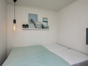 A bedroom with a single bed, a hanging light fixture, and a shelf with framed pictures and plants.