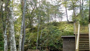 A wooden cabin with a wooden staircase leading up to a deck, surrounded by dense forest and a dirt path. - 6 Person Holiday Home in Lysekil (Lysekil)