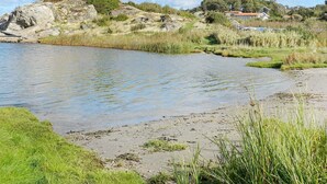 A riverbank with a rocky outcrop, grassy areas, and a distant building. - 6 Person Holiday Home in Lysekil (Lysekil)