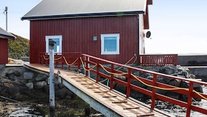A red wooden building with a metal roof, a wooden dock with a red railing, and a stone wall in the background. - 6 Person Holiday Home in Brekstad (Orland)