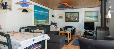 Een gezellige woonkamer met houten plafond, een eettafel met stoelen, een bank, een televisie en een open haard.