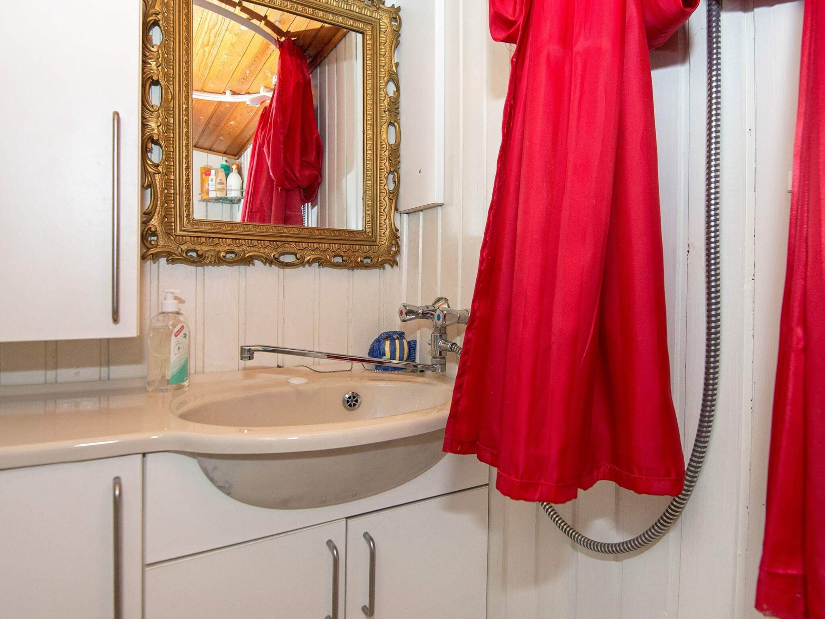 A bathroom with a sink, mirror, and red towel hanging on a rack.