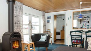 A cozy living room with a wood-burning stove, a sofa, a dining table with chairs, and a kitchen visible through an open doorway. - 5 Person Holiday Home in Thyboron (Thyborøn)
