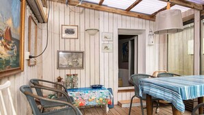 A covered outdoor dining area with wooden flooring, two tables with blue-striped tablecloths, wicker chairs, and a ceiling with exposed beams. - 5 Person Holiday Home in Thyboron (Thyborøn)