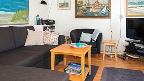A living room with a sofa, a coffee table, a TV, and paintings on the wall. - 5 Person Holiday Home in Thyboron (Thyborøn)