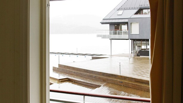 A view from a window overlooking a wooden deck with a metal railing, leading to a building with a sloped roof and a balcony. - 6 Person Holiday Home in Holmsbu (Asker)