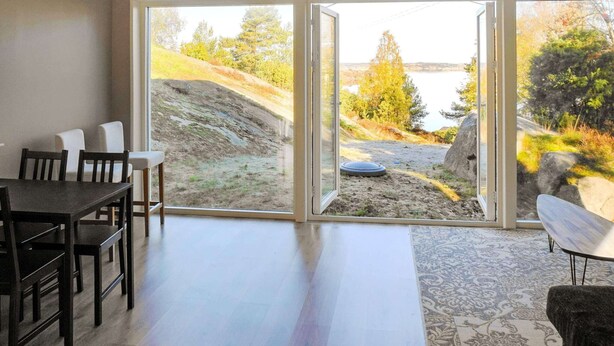 Una habitación con una mesa de comedor y sillas, un amplio ventanal corredero que da a una vista panorámica con un lago y colinas.