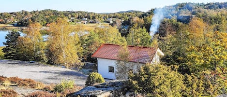 A small white building with a red roof surrounded by autumn foliage and a lake in the background.